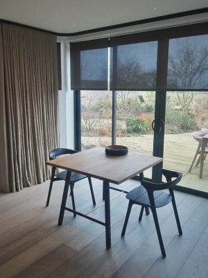 Roller Blinds This image shows black semi-transparent roller blinds, fitted onto large sliding doors looking out onto a garden with decking.