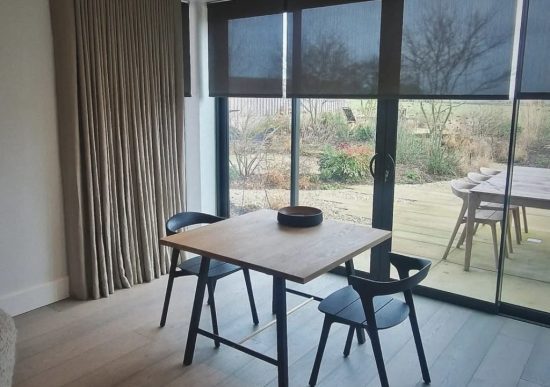 This image shows black semi-transparent roller blinds, fitted onto large sliding doors looking out onto a garden with decking.
