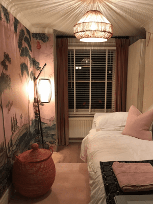 Venetian blinds This image shows white Venetian blinds in a dimly lit room with a small bed and a Japanese mural painted on the wall.