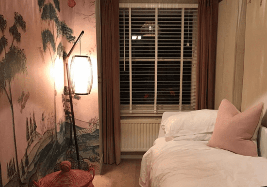 This image shows white Venetian blinds in a dimly lit room with a small bed and a Japanese mural painted on the wall.
