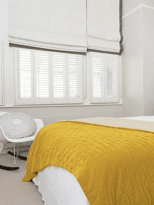 Shutters and Roman Blinds This image shows white shutters fitted onto bedroom windows, half covered by white and grey roman blinds.