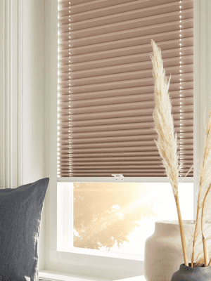 Perfect Fit Blinds This image shows sand coloured perfect-fit honeycomb blinds fitted onto a white window frame with the sun shining through.